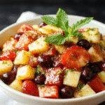 Colorful summer fruit salad with slices of watermelon, strawberries, blueberries, pineapple, and mint leaves arranged in a glass bowl.