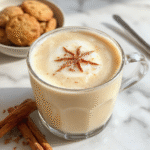 A steaming glass of vanilla cinnamon latte topped with whipped cream and a sprinkle of cinnamon, served on a rustic wooden table with cinnamon sticks and vanilla beans, showcasing a warm and inviting beverage with rich caramel hues and frothy textures.