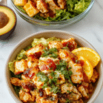 Colorful chicken burrito bowls featuring diced grilled chicken, vibrant red and green bell peppers, black beans, corn, and fresh cilantro on a white plate, topped with shredded cheese and a squeeze of lime, styled with a rustic wooden background