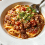 A close-up of a creamy ground beef orzo dish plated in a white bowl, featuring tender orzo pasta mixed with juicy ground beef, vibrant red tomato sauce, and a sprinkle of fresh herbs, all styled on a rustic wooden table.